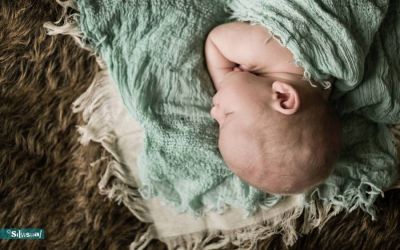Slapende pasgeboren baby in mintgroene wrap op bruin vachtje tijdens newbornshoot bij Silvisual in Waalwijk