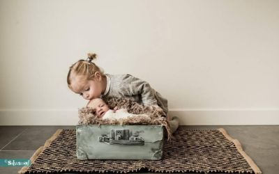 Newborn fotoshoot met pasgeboren baby in koffertje en kind dat er liefdevol overheen leunt